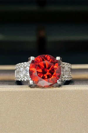 Crimson solitaire ring with pave band, featuring a large round red stone and small clear stones.
