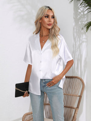 White satin collared shirt with button front and short sleeves, styled with jeans and a clutch.
