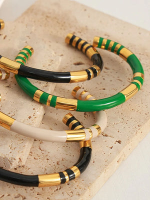 Striped enamel and gold bangle bracelets in dark green, black, and cream.