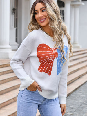 White knit sweater with a graphic red and blue bow pattern.