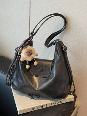 Black slouchy pu leather shoulder bag with button flap closure and fuzzy charm.
