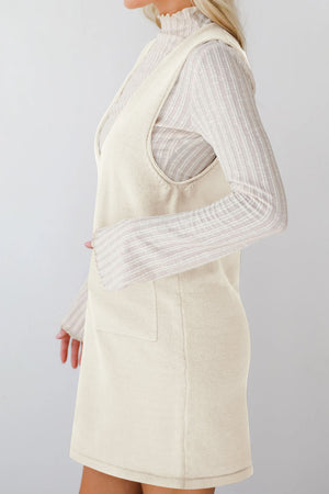 Cream sleeveless knit pocket dress with V-neck, styled over a ribbed turtleneck.