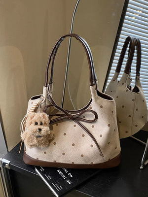 Tan polka dot shoulder bag with brown trim, bow detail, and fluffy dog charm.