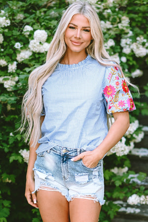 Light blue gingham blouse with embroidered floral sleeves and ruffled neckline.
