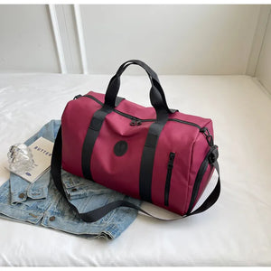 Burgundy duffel bag with black contrast straps and zipper details, shown with a denim jacket.