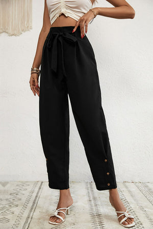 Black paperbag waist trousers with tie belt and buttoned hemline detail.