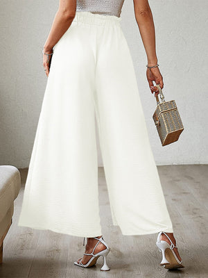 White pleated palazzo pants with a high waist and wide leg, featuring a subtle slit.