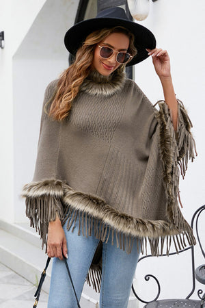 Taupe knit poncho with faux fur trim and fringe details, featuring a cable knit pattern.