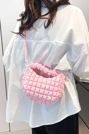 Pink padded crescent crossbody bag with sculptural texture and ruched detail.