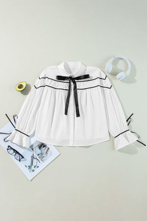 White blouse with black piped trim and bow detail, long sleeves with ruffled cuffs.