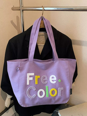 Lavender canvas shoulder bag with textured letter applique spelling Free. Color.
