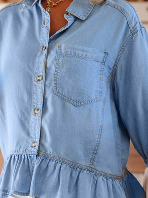 Light blue chambray button-down maternity shirt with chest pocket and ruffled hem.