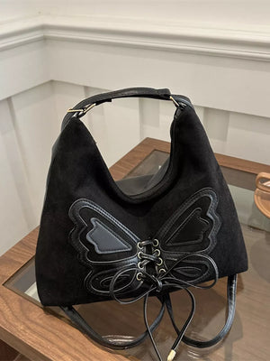 Black suede half-moon shoulder bag with butterfly embellishment and lace-up detail.