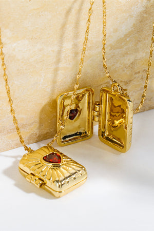 Gold locket pendant necklace with red heart detail and chain.