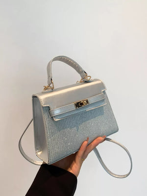 Silver glitter textured mini crossbody bag with top handle and gold clasp.
