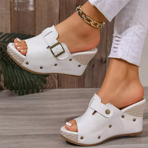 White wedge sandals with decorative accents and buckle detail.