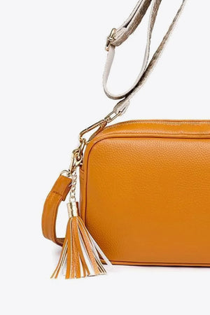 Textured crossbody bag in orange with a multi-color tassel detail and adjustable strap.