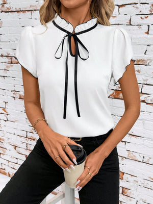 White frilled tie-neck blouse with black trim and short sleeves.