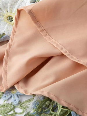 Maxi dress detail: peach fabric with embroidered floral appliqué in blue and green.