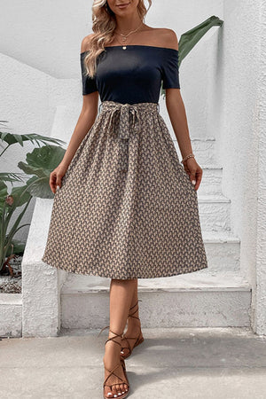 Black off-shoulder midi dress with a patterned A-line skirt and tie waist.