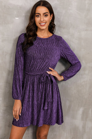 Violet textured pleated mini dress with long sleeves and a tie waist.