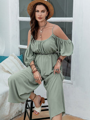 Sage off-shoulder jumpsuit with gathered waist, puff sleeves, and wide legs.