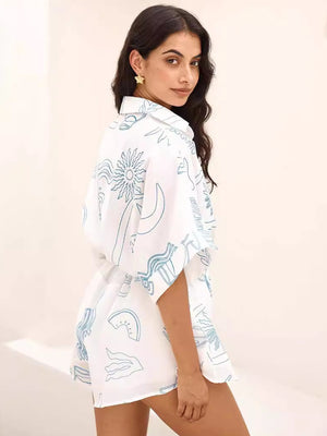 White linen romper with abstract cocktail print, short sleeves, and tie waist detail.