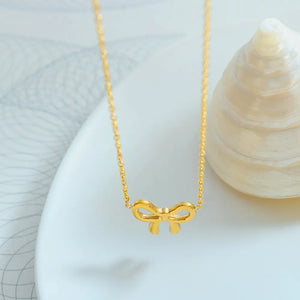Delicate gold bow pendant necklace on a fine chain.