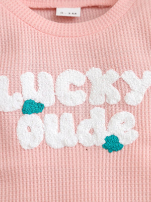 Pink waffle knit baby one-piece with textured white Lucky Dude lettering and teal accents.