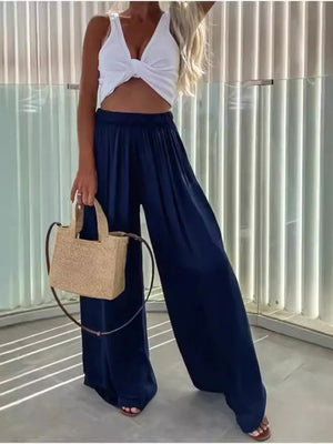 Dark blue maternity pants with paperbag waist and wide legs, styled with a white crop top and straw bag.