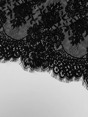 Black lace trim detail with scalloped edge and fringe on a dress.