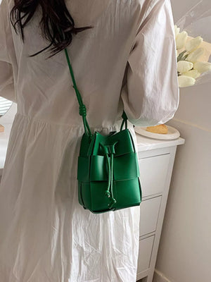 Green woven mini bucket bag with drawstring closure and crossbody strap.