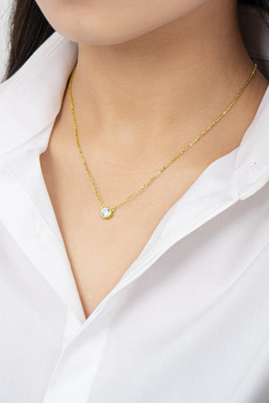 Gold solitaire moissanite bezel necklace on a woman wearing a white shirt