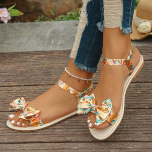 Floral bowknot flat sandals in beige with colorful print and ankle strap.