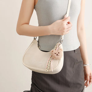 Mini crescent shoulder bag in cream with a fuzzy bear charm and adjustable strap.