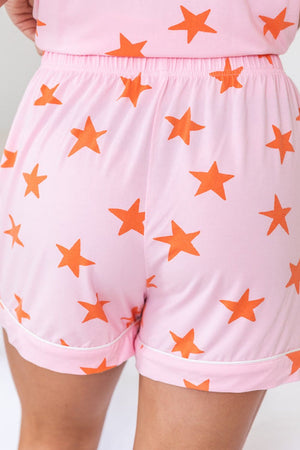 Blush pink pajama shorts with orange stars and white piping.