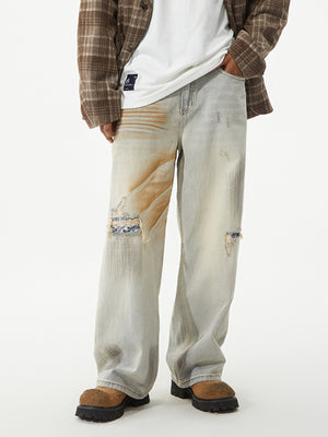 Distressed wide-leg jeans in light wash denim with unique tan patches and ripped details.