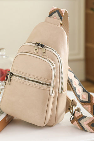 Geometric strap sling bag in cream with multiple zippered pockets and a colorful woven strap.