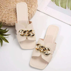 White slide sandals with textured straps and gold chain embellishment.