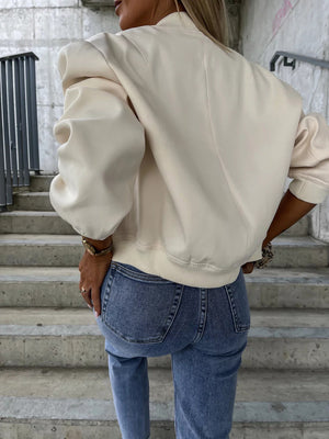 Beige faux leather bomber jacket with sculpted sleeves and ribbed cuffs, styled with jeans.