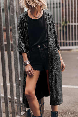 Black sequin kimono jacket with open front and wide sleeves, worn over black top and shorts.