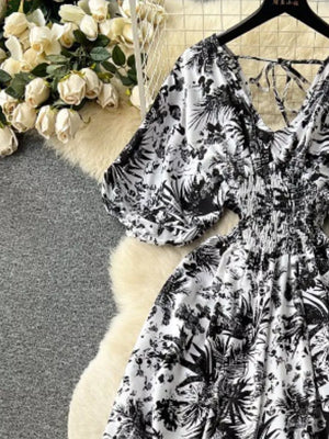 Tropical print smocked wide-leg romper with tie back detail and puff sleeves.