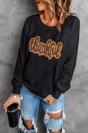 Black crewneck sweatshirt with sequin "thankful" graphic.