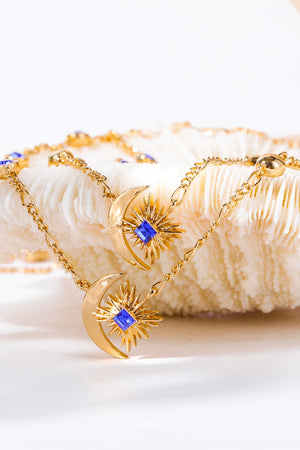 Gold celestial necklace with sunburst and crescent moon charms featuring blue square gems.