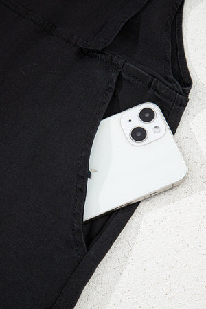 Black denim romper with adjustable straps and a pocket holding a smartphone.