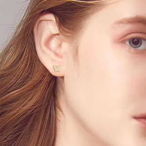 Gold moissanite butterfly stud earrings with clear stones, shown on ear.