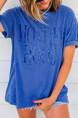 Blue oversized graphic tee with "MOTHERHOOD" text, cuffed sleeves, and raw hem shorts.