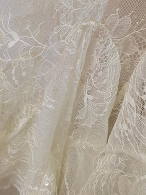 White floral lace dress fabric with ruffle detail and subtle sequins.