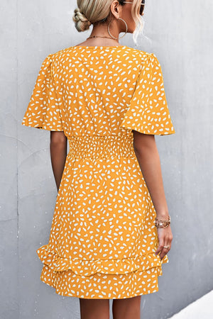 Mustard mini dress with white speckle print, flutter sleeves, smocked waist, and ruffled hem.