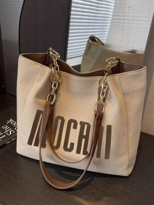 Textured canvas shoulder bag in beige with brown lettering and gold chain accents.